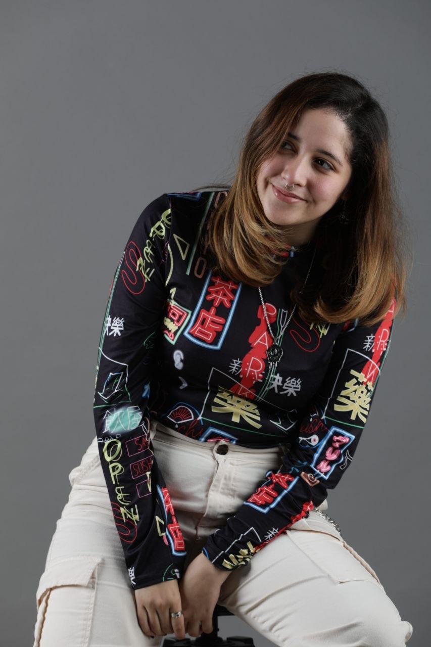 Retrato de Chiqui sonriendo, con camiseta negra de estampado neón y pantalón blanco